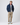 Model wearing navy bomber jacket layered over light grey sweater with beige trousers and blue sneakers.