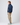 Side profile of man in navy jacket with ribbed cuffs and hem, styled with beige trousers and sneakers.