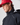 Side profile of model wearing the Men's Dynamic Jacket in black with a red Henri-Lloyd cap, hood down, highlighting high collar and taped seams.