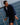 A man wearing a navy blue zip-up fleece jacket and matching shorts stands on a sailboat with the ocean in the background.