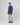 Person wearing a navy waterproof jacket, beige trousers, brown shoes, and a navy cap, standing against a white background.