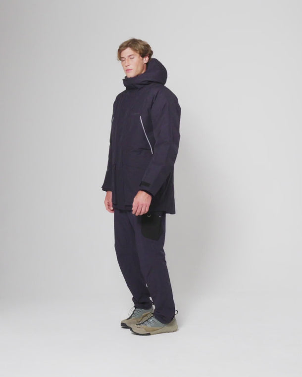 Model wearing a men's waterproof parka jacket and matching trousers, standing in a studio setting.