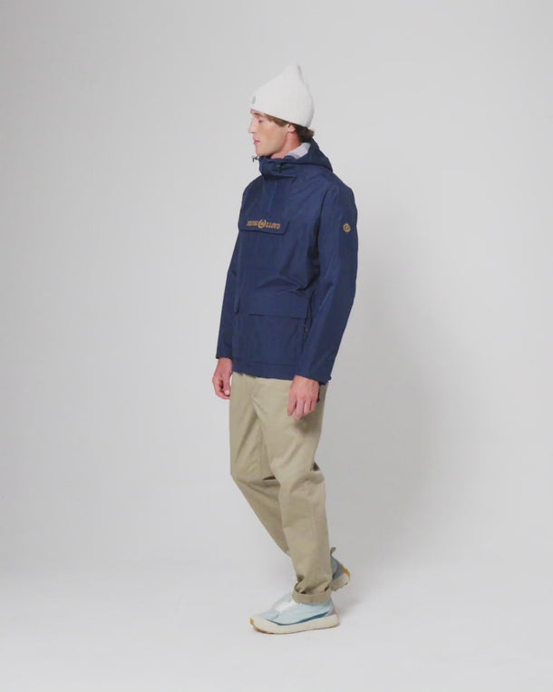 Person wearing Henri-Lloyd waterproof jacket with white beanie and beige trousers in studio setting